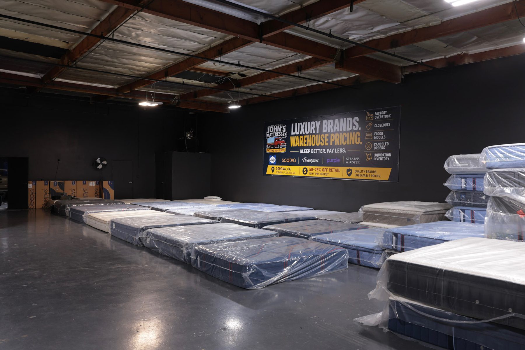 Warehouse interior with the John's Mattresses banner reading Luxury Brands, Warehouse Pricing